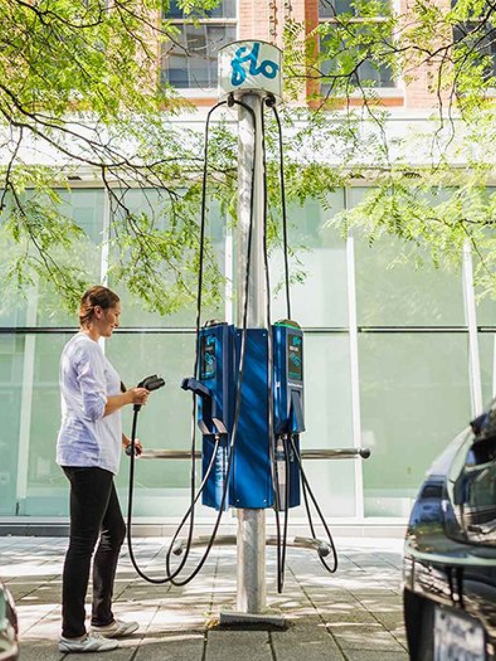 Personne branchant une voiture électrique à une borne de recharge FLO entre deux véhicules stationnés.
