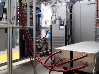 Équipement industriel de test avec de nombreux câbles rouges et orange connectés à un module métallique posé sur une plateforme.