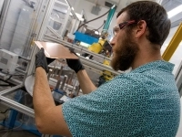 Personne manipulant une plaque métallique dans un environnement industriel équipé de machinerie.
