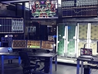Salle de contrôle remplie d’écrans affichant des données techniques et des schémas électroniques, avec des postes de travail informatiques.