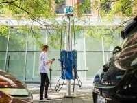 Personne branchant une voiture électrique à une borne de recharge FLO entre deux véhicules stationnés.