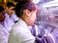 Personnes en sarraus de laboratoire travaillant dans une enceinte de manipulation équipée de gants intégrés.